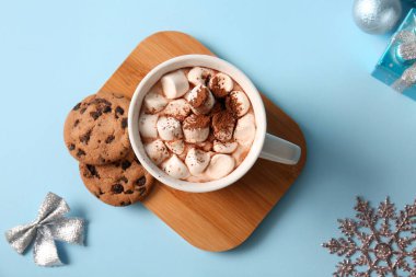 Bir fincan sıcak kakao, marşmelov ve mavi arka planda tatlı kurabiyeler.