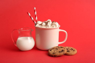 Bir fincan sıcak kakao, marşmelov ve kırmızı arka planda tatlı kurabiyeler.