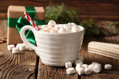 Bir fincan kremalı sıcak kakao, tatlı waffle ve ahşap arka planda hediye paketi.