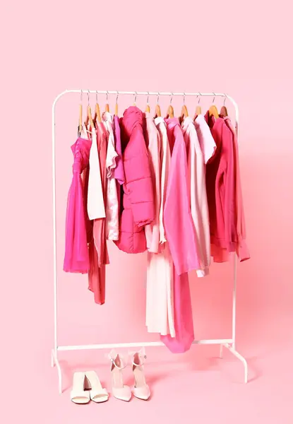 Rack with pink clothes and shoes on color background