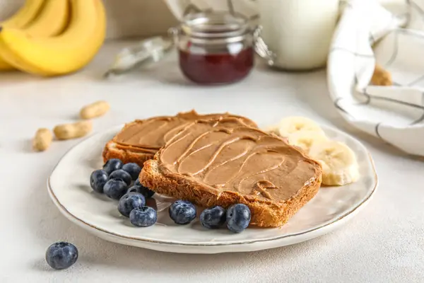 Plate of toasts with peanut butter, banana and blueberries on white background