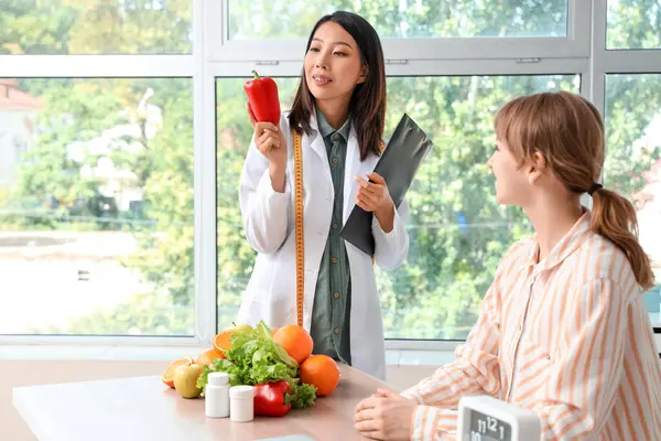 Female Asian nutritionist with healthy food and patient in office