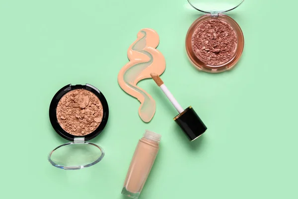 Bottle of makeup foundation with sample and decorative cosmetics on green background