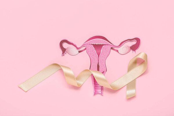 Paper uterus with beige ribbon on pink background. Cancer awareness concept