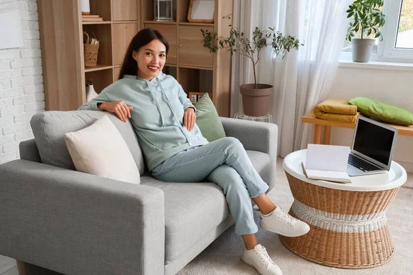 Şık kapüşonlu güzel Asyalı kadın evdeki kanepede oturuyor.