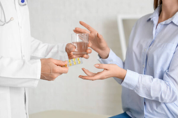 Male doctor giving pills and water to pregnant woman in clinic, closeup
