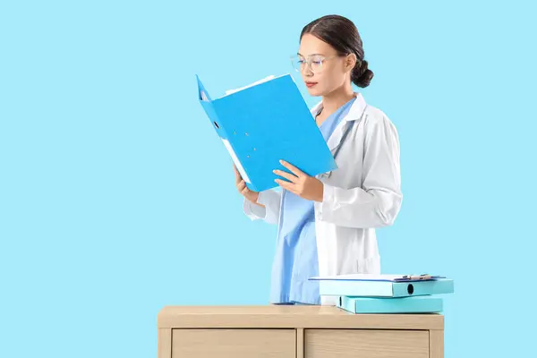 Female Asian doctor with folder on blue background