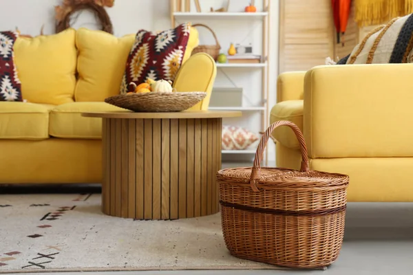 Interior of living room with yellow sofa, wooden coffee table, wicker basket and pumpkins