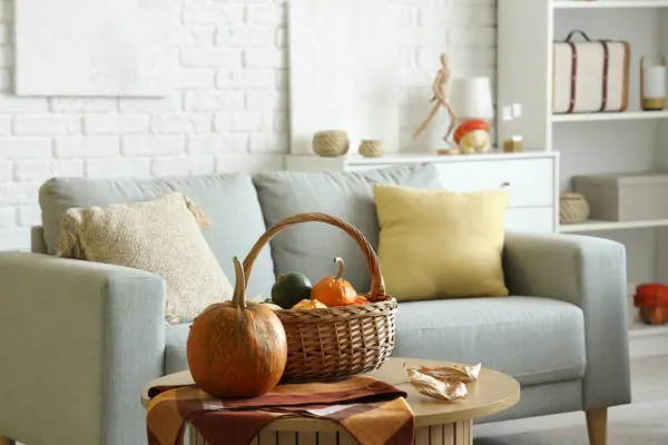 Basket with pumpkins and autumn leaves on table in living room