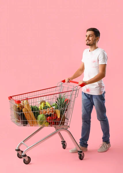 Young man with shopping cart on pink background