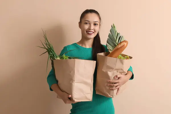 Young Asian woman with shopping bags full of fresh food on brown background