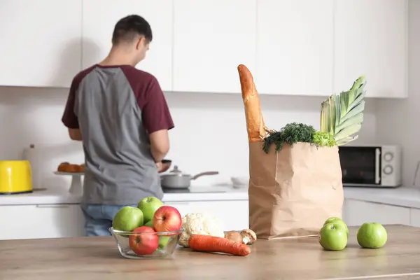 Grocery bag with fresh vegetables and fruits on table in kitchen