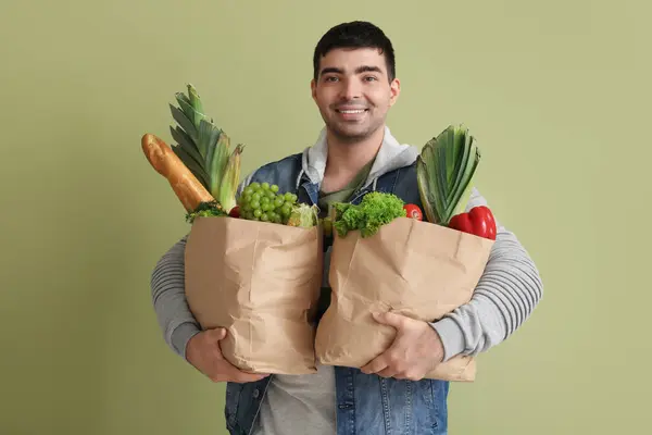Young man with grocery bags on green background