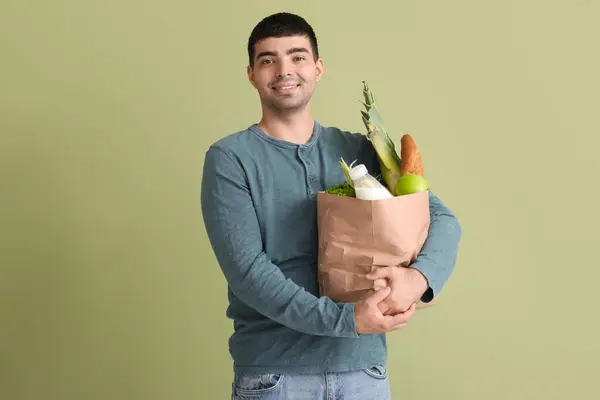 Young man with grocery bag on green background
