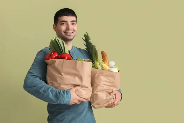Young man with grocery bags on green background