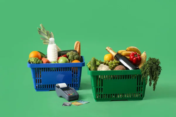 Shopping baskets full of food with payment terminal and credit cards on green background