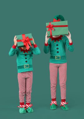 Yeşil arka planda Noel hediyesi kutuları olan elf kostümlü şirin çocuklar.