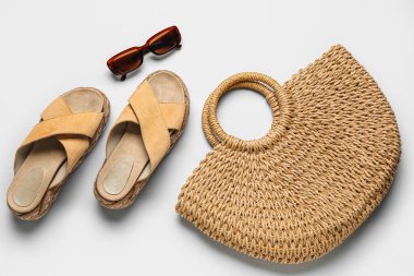 Hasır çantalı bej sandaletler ve gri arka planda güneş gözlükleri.