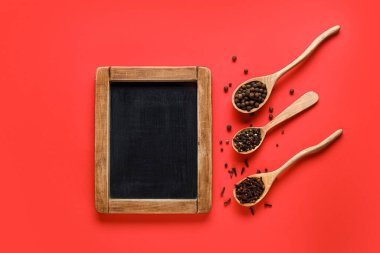Kırmızı zemin üzerinde boş karatahta ve kaşık dolusu baharat içeren kompozisyon