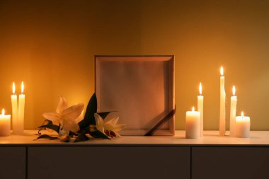 Boş cenaze çerçevesi, yanan mumlar ve karanlık odada dolapta zambak çiçekleri.