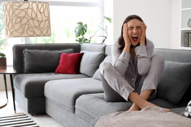 Güzel, genç, korkmuş bir kadın kanepede oturuyor ve oturma odasında bağırıyor.