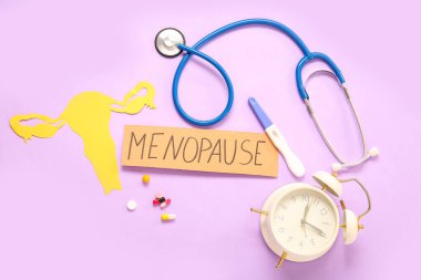 Kağıt rahim, hap, hamilelik testi, steteskop ve pembe zemin üzerindeki saat ile MENOPAUSE kelime