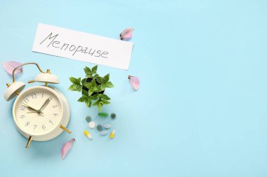 Word MENOPAUSE with alarm clock, pills and petals on blue background clipart