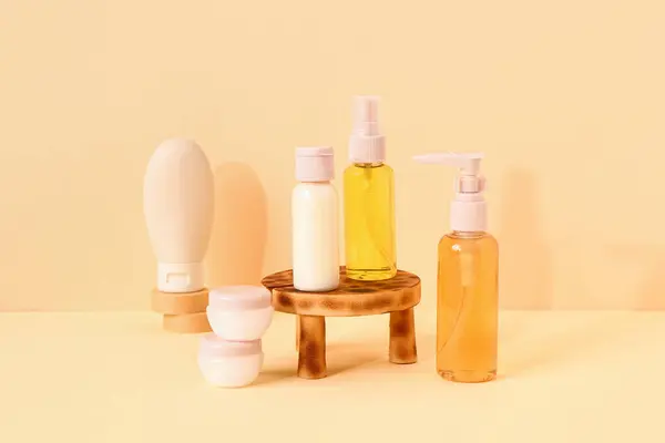 Stand with set of travel cosmetic products on pale yellow background