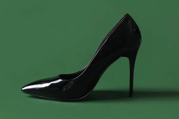 Stylish black high heel on green background