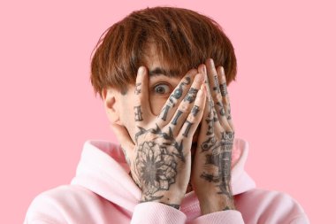 Pembe arka planda dövmeli genç bir adam.