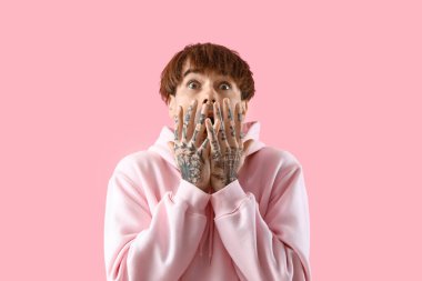 Pembe arka planda dövmeli genç bir adam.