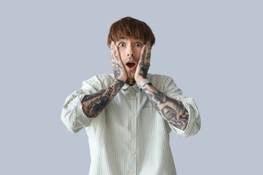 Gri arka planda dövmeli genç bir adam.