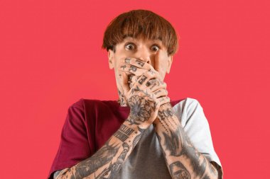 Kırmızı arka planda dövmeli, korkmuş genç bir adam.