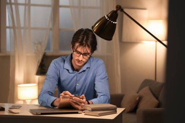 Gece ofiste çalışan defterli genç bir işadamı.