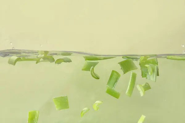 Cut aloe leaves in water on green background