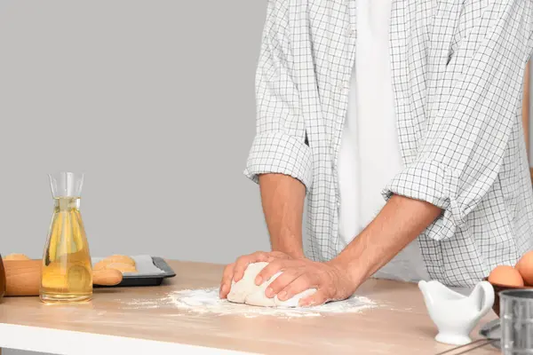 Genç adam mutfaktaki masada taze çörekler için hamur hazırlıyor.
