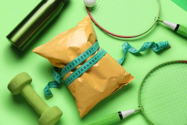 Sağlıklı atıştırmalıklar ve yeşil arka planda farklı spor ekipmanları olan kompozisyon