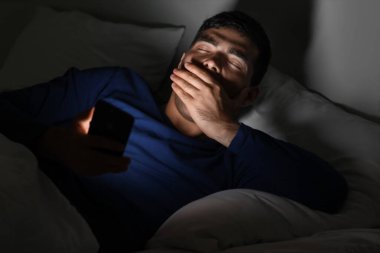 Uykulu genç adam geceleri cep telefonu kullanıyor.