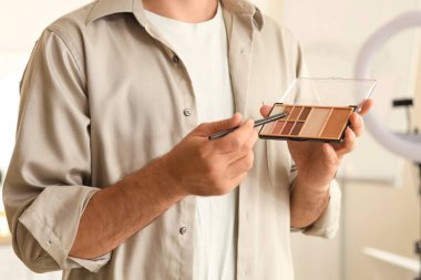 Soyunma odasında fırça ve göz farı olan erkek makyaj sanatçısı, yakın plan.