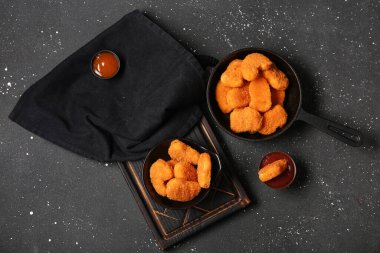 Kızartma tavası ve siyah arka planda soslu bir kase lezzetli nugget.