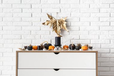 Beyaz tuğla duvarın yanında içi balkabağı, koni ve mum dolu çekmeceler.