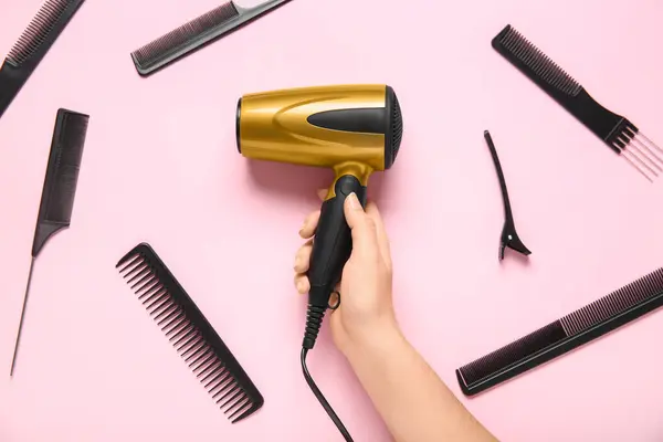 Female hand with hair dryer and combs on pink background