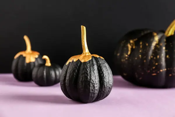 Painted pumpkins on purple table near black wall