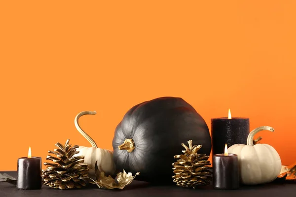 Painted pumpkins with golden cones, leaves and candles on black table near orange wall