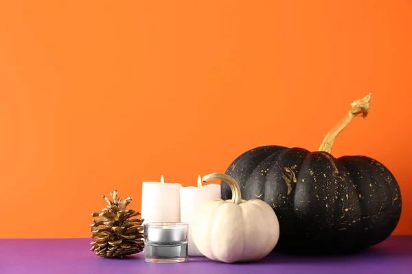 Painted pumpkins with golden cone and candles on purple table near orange wall
