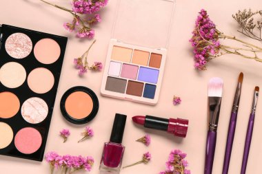 Farklı makyaj ürünleri ve pembe arka planda güzel çiçekler olan kompozisyon