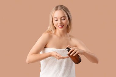 Genç sarışın kadın bej arka planda duş aldıktan sonra saç kremi sürüyor.