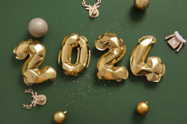 Yeşil arka planda Noel süslemeleri olan folyodan yapılmış 2024 numaralı figür.