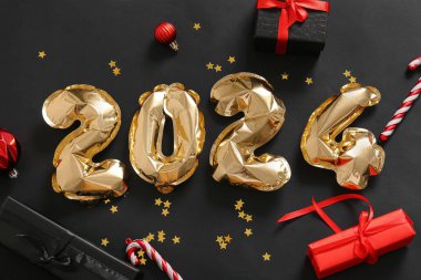 Noel topları, baston şekerler ve siyah arka planda hediye kutuları olan folyodan yapılmış 2024 model.