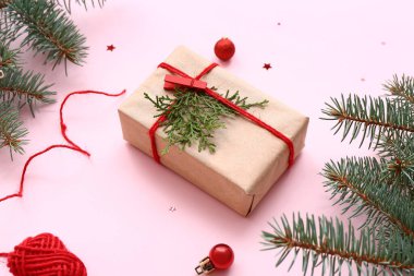 Noel ağacı dalları ve pembe arka planda topları olan bir hediye kutusu.